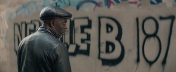 Movie still from “The Gambler” (2014), directed by Rupert Wyatt – A man in a leather jacket and hat standing in front of a wall with graffiti on it; Close Up shot, Over the shoulder angle