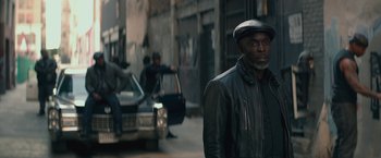 Movie still from “The Gambler” (2014), directed by Rupert Wyatt – A man wearing a leather jacket and a hat standing in front of a car; Medium shot, Over the shoulder angle