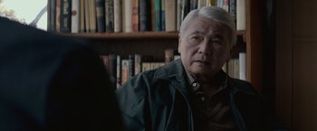 Movie still from “The Gambler” (2014), directed by Rupert Wyatt – An older man sitting in front of a book shelf; Close Up shot, Over the shoulder angle