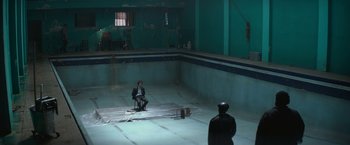 Movie still from “The Gambler” (2014), directed by Rupert Wyatt – A man sitting on a chair next to another man in an empty swimming pool; Extreme Wide shot, High angle