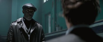 A man wearing a hat and a leather jacket looking at himself in the mirror