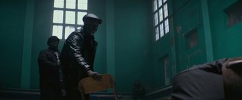 Movie still from “The Gambler” (2014), directed by Rupert Wyatt – A man in a leather jacket and hat holding onto a chair; Medium shot, Low angle