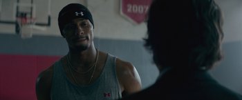 Movie still from “The Gambler” (2014), directed by Rupert Wyatt – A man in a black hat and a gray tank top is smiling; Close Up shot, Over the shoulder angle