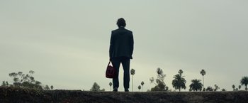 Movie still from “The Gambler” (2014), directed by Rupert Wyatt – A man standing on a hill holding a red purse; Extreme Wide shot, Low angle