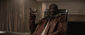 Movie still from “The Gambler” (2014), directed by Rupert Wyatt – A man sitting in a chair holding a glass of whiskey; Medium shot, Low angle