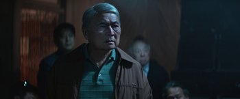 Movie still from “The Gambler” (2014), directed by Rupert Wyatt – An older man wearing a green shirt and a brown jacket; Close Up shot, Over the shoulder angle