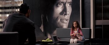 A young girl sitting in front of a large poster of a man