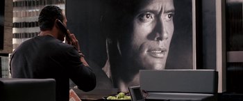 Movie still from “The Game Plan” (2007), directed by Andy Fickman – A man sitting in front of a large picture of a man; Close Up shot, Over the shoulder angle