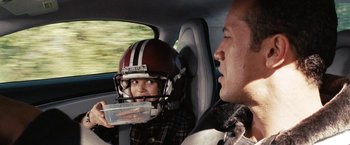 Movie still from “The Game Plan” (2007), directed by Andy Fickman – A man and a child in a car with a football helmet on; Close Up shot, Over the shoulder angle
