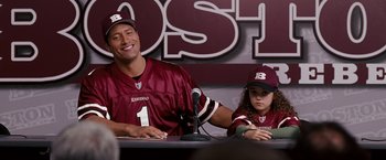 Movie still from “The Game Plan” (2007), directed by Andy Fickman – A man sitting next to a little girl in front of microphones; Medium shot, Over the shoulder angle