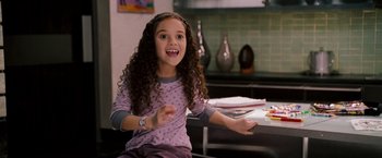 Movie still from “The Game Plan” (2007), directed by Andy Fickman – A little girl sitting at a table with her arms outstreched; Medium shot, High angle