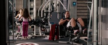 Movie still from “The Game Plan” (2007), directed by Andy Fickman – A man sitting on a bench in a gym; Wide shot, Overhead angle