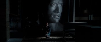 Movie still from “The Game Plan” (2007), directed by Andy Fickman – A man sitting on the ground in front of a large portrait; Wide shot, High angle