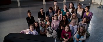 Movie still from “The Game Plan” (2007), directed by Andy Fickman – A group of people and a dog sitting in front of a wall; Wide shot, High angle