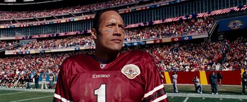 Movie still from “The Game Plan” (2007), directed by Andy Fickman – A man in a football jersey standing in front of a crowd; Close Up shot, High angle