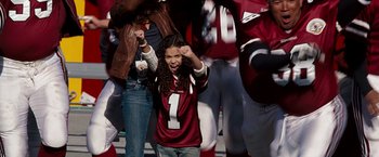 Movie still from “The Game Plan” (2007), directed by Andy Fickman – A young girl in a football jersey holding her hands in the air; Medium shot, High angle