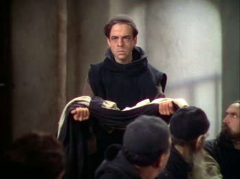 Movie still from “The Garden of Allah” (1936), directed by Richard Boleslawski – A man in a monk's outfit is holding a black cloth; Medium shot, Over the shoulder angle