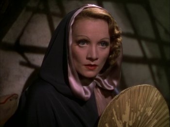 Movie still from “The Garden of Allah” (1936), directed by Richard Boleslawski – A person holding a fan and wearing a hood; Close Up shot, High angle