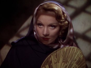 Movie still from “The Garden of Allah” (1936), directed by Richard Boleslawski – A woman with a scarf around her head and a fan; Close Up shot, Over the shoulder angle