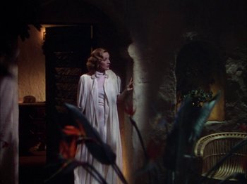 Movie still from “The Garden of Allah” (1936), directed by Richard Boleslawski – A woman in a white dress standing next to a wall; Wide shot, Over the shoulder angle