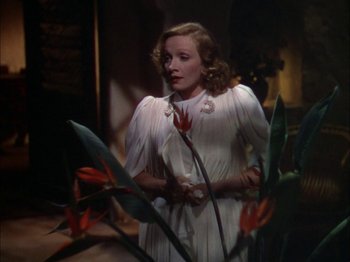 Movie still from “The Garden of Allah” (1936), directed by Richard Boleslawski – A woman in a white dress standing next to flowers; Medium shot, Low angle