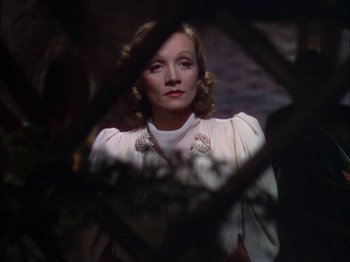 Movie still from “The Garden of Allah” (1936), directed by Richard Boleslawski – A woman in a white jacket looking at the camera through a tree branch; Medium shot, Low angle