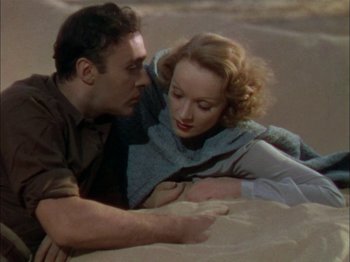 Movie still from “The Garden of Allah” (1936), directed by Richard Boleslawski – A man and a woman laying in the sand together; Medium shot, High angle