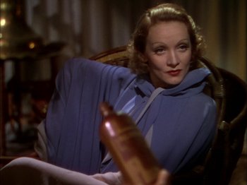 Movie still from “The Garden of Allah” (1936), directed by Richard Boleslawski – A woman sitting in a chair holding a bottle of wine; Medium shot, Low angle