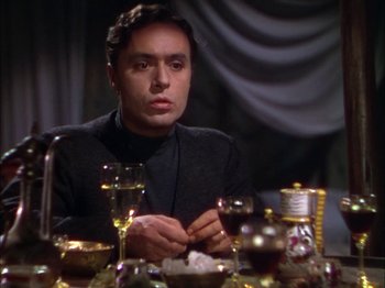 Movie still from “The Garden of Allah” (1936), directed by Richard Boleslawski – A man sitting at a dinner table with a glass of wine; Medium shot, Low angle