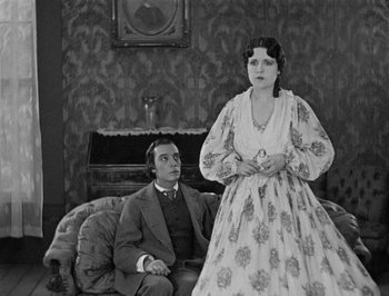 Movie still from “The General” (1926), directed by Buster Keaton – A man and a woman sitting on a couch in a room; Medium shot, Low angle