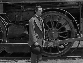 Movie still from “The General” (1926), directed by Buster Keaton – A black and white photo of a man standing next to a train; Medium shot, High angle