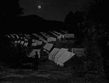 Movie still from “The General” (1926), directed by Buster Keaton – A man standing in front of tents at night; Extreme Wide shot, High angle
