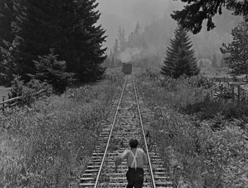 Movie still from “The General” (1926), directed by Buster Keaton – A man standing on a train track next to a forest; Extreme Wide shot, High angle