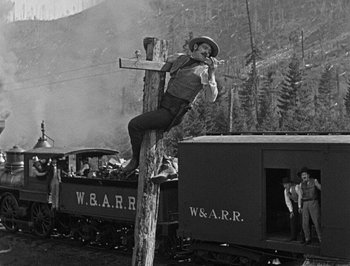 Movie still from “The General” (1926), directed by Buster Keaton – An old photo of a man hanging on to a wooden pole; Wide shot, Low angle