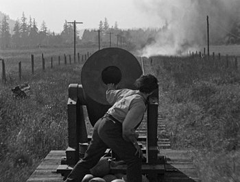 Movie still from “The General” (1926), directed by Buster Keaton – A man standing next to a train on a train track; Wide shot, Low angle