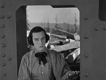 Movie still from “The General” (1926), directed by Buster Keaton – A man with a bow tie is sitting in a train car; Medium shot, High angle