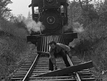 Movie still from “The General” (1926), directed by Buster Keaton – A man standing on a train tracks near a train; Wide shot, High angle