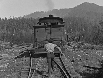 Movie still from “The General” (1926), directed by Buster Keaton – A man walking across a train tracks near a forest; Wide shot, High angle