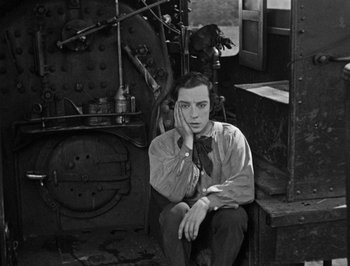 Movie still from “The General” (1926), directed by Buster Keaton – A man sitting on a bench next to an old train car; Medium shot, High angle