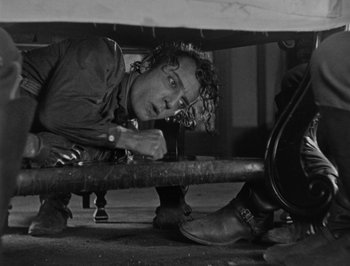 Movie still from “The General” (1926), directed by Buster Keaton – A man leaning on a bench under a table; Medium shot, Low angle