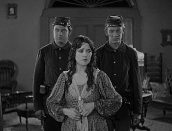 Movie still from “The General” (1926), directed by Buster Keaton – A black and white photo of a woman in front of two other men; Medium shot, Over the shoulder angle