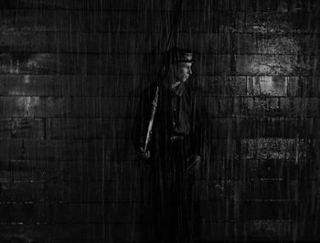 Movie still from “The General” (1926), directed by Buster Keaton – A man holding a rifle standing next to a wall; Wide shot, Low angle