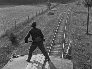 Movie still from “The General” (1926), directed by Buster Keaton – A man standing on top of a train track; Wide shot, Low angle