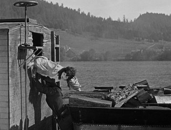 Movie still from “The General” (1926), directed by Buster Keaton – A man standing next to a pile of wood on top of a boat; Wide shot, Low angle