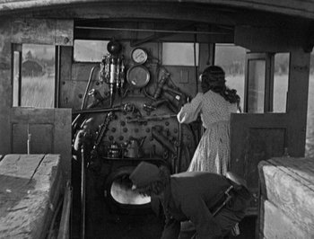 Movie still from “The General” (1926), directed by Buster Keaton – A woman and a man working on an old train engine; Wide shot, High angle