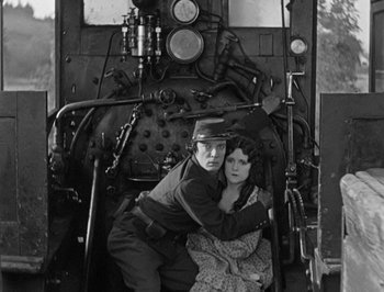 Movie still from “The General” (1926), directed by Buster Keaton – A man and a woman sitting on the front of an old train; Medium shot, High angle