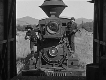 Movie still from “The General” (1926), directed by Buster Keaton – A black and white photo of two men standing next to an old train; Wide shot, Low angle