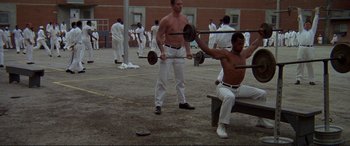 Movie still from “The Getaway” (1972), directed by Sam Peckinpah – A man is sitting on a park bench lifting a barbell; Wide shot, High angle