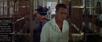 Movie still from “The Getaway” (1972), directed by Sam Peckinpah – A man standing next to another man in a jail cell; Medium shot, Over the shoulder angle
