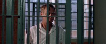 Movie still from “The Getaway” (1972), directed by Sam Peckinpah – A man standing behind bars in a jail cell; Medium shot, Low angle